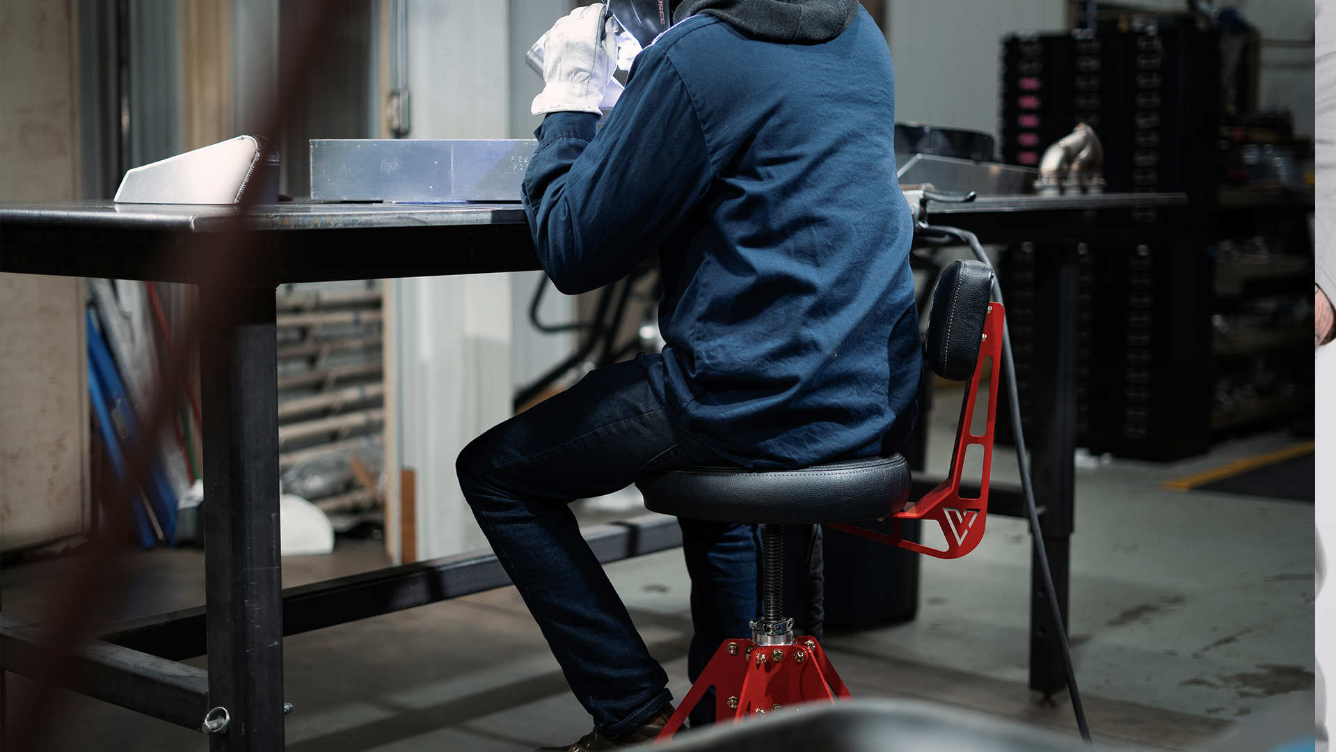 person sitting in red and block shop chair working on car in garage