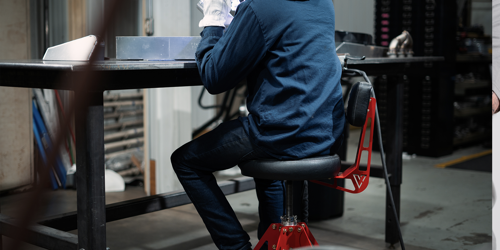person sitting in red and block shop chair working on car in garage