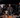 four guys in a studio standing around a table in discussion. there are bottles of whiskey and microphones on the table