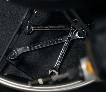 Black tool tray on black chair holding three silver wrenches